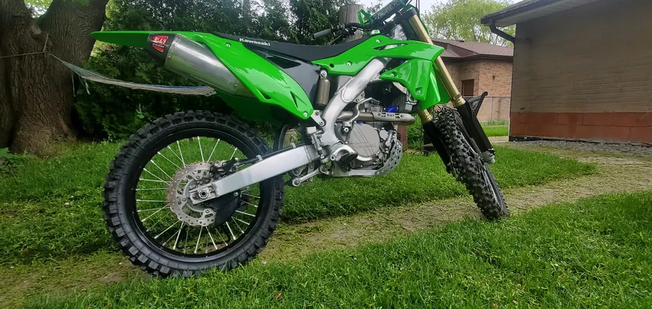 Finished green Kawasaki four-stroke dirt bike parked beside a walkway