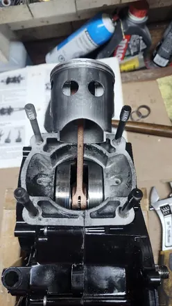 Vintage two-stroke piston above the connecting rod, with the service manual open behind it