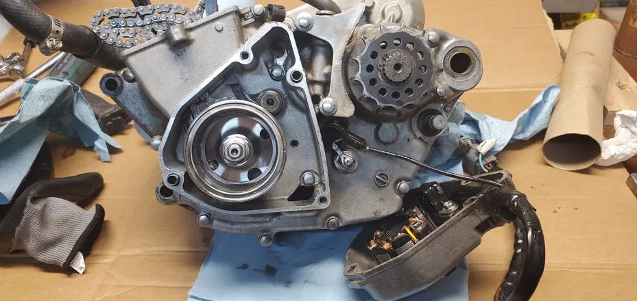 Four-stroke engine with the side cover off during teardown, showing the flywheel and gears