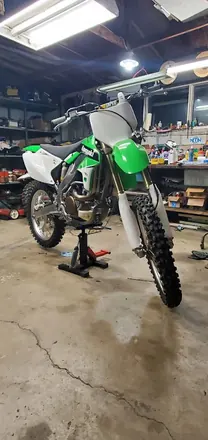 Finished green and white Kawasaki dirt bike on a stand in the shop